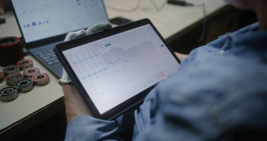 Adam, Dijital Tablet ve Laptop kullanarak Gerçek zamanlı borsa grafiklerini kontrol ediyor. Çalışanların atölyede çalışma saatleri sırasında yatırım yapması, İş ve Çevrimiçi Ticaret 'i birleştirmesi. Kapat..