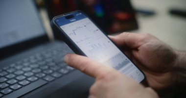 Adam Smartphone ve Laptop 'ta Gerçek zamanlı borsa grafiklerini kontrol ediyor Tablet' te Online Ticaret Dersi izliyor. Çalışanların atölyede çalışma saatlerinde yatırım yapmaları. Kapat..