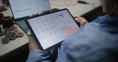 Adam, Dijital Tablet ve Laptop kullanarak Gerçek zamanlı borsa grafiklerini kontrol ediyor. Çalışanların atölyede çalışma saatleri sırasında yatırım yapması, İş ve Çevrimiçi Ticaret 'i birleştirmesi. Kapat..