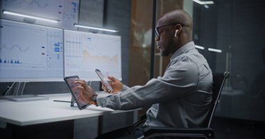 Afro-Amerikan Finansal Analizci, Gerçek-Zaman Hisselerini Analiz Etme, Dijital Tablet, Akıllı Telefon ve Bilgisayar Piyasa Grafikleri ve Çoklu-Monitör Çalışma İstasyonu. Yatırım Bankası Ofisinde İşadamı.