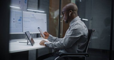 Afro-Amerikan Finansal Analizci, Gerçek-Zaman Hisselerini Analiz Etme, Dijital Tablet, Akıllı Telefon ve Bilgisayar Piyasa Grafikleri ve Çoklu-Monitör Çalışma İstasyonu. Yatırım Bankası Ofisinde İşadamı.