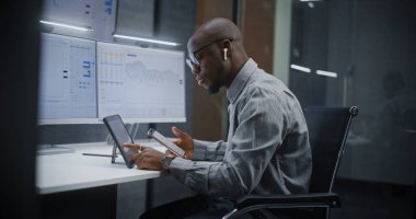 Afro-Amerikan Finansal Analizci, Gerçek-Zaman Hisselerini Analiz Etme, Dijital Tablet, Akıllı Telefon ve Bilgisayar Piyasa Grafikleri ve Çoklu-Monitör Çalışma İstasyonu. Yatırım Bankası Ofisinde İşadamı.