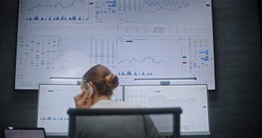 Çoklu Monitör Çalışma İstasyonu, Gerçek zamanlı borsa ve borsa grafiklerinin izlenmesi ve telefonda konuşulması ile bilgisayar üzerinde çalışan kadın finans analisti. Gece Finans Ajansı Ofisi 'ndeki iş kadını