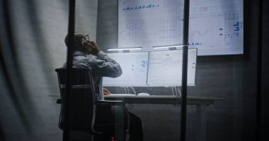 Multi-Monitor Workstation ile bilgisayar üzerinde çalışan finansal analist, Gerçek zamanlı borsa grafiklerini analiz eden, telefonda konuşan. Afrikalı Amerikalı İşadamı Geceleri Ofiste Çalışıyor.