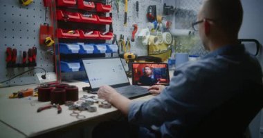 Gerçek zamanlı borsa çizelgelerini kontrol eden adam dizüstü bilgisayarını kullanarak dijital tablet üzerinde online ticaret dersi izliyor. Çalışanların atölyede mesai saatlerinde uzaktan ticaret eğitimi alması.