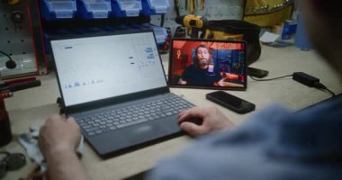 Gerçek zamanlı borsa grafiklerini kontrol eden adam dizüstü bilgisayarını kullanıyor, dijital tabletten online ticaret dersi izliyor. Çalışanların Mesai saatlerinde atölyede uzaktan öğrenme ticareti. Kapat..