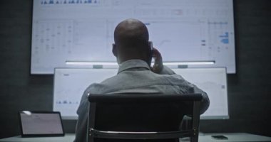 Multi-Monitor Workstation ile bilgisayar üzerinde çalışan Finansal Analizci, Gerçek zamanlı Borsa Çizelgelerini İzleyen, Telefonda Konuşan. Afrikalı Amerikalı İşadamı Geceleri Ofiste Çalışıyor.