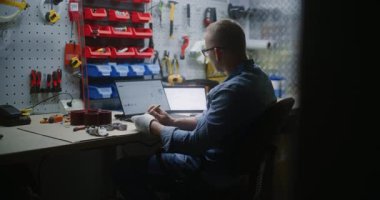 El işi yapan, gerçek zamanlı hisse senetlerini izleyen, dizüstü bilgisayardaki ve tablet bilgisayardaki borsa grafiklerini değiştiren bir zanaatkar. Atölyede İş Gününde Yatırım Yapan, Çevrimiçi Ticaretle Çalışmayı Birleştiren Adam.
