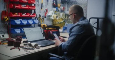 Eş zamanlı borsa grafiklerini kontrol eden tamirci dizüstü bilgisayar ve telefon kullanarak dijital tablet üzerine online ticaret dersi izliyor. Adam atölyede uzaktan ticaret eğitimi alıyor..