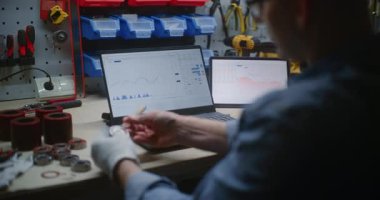 El işi yapan tamirci, gerçek zamanlı hisse senedi kontrolü, dizüstü bilgisayar ve dijital tabletteki borsa grafikleri. Atölyede Çalışma Saatlerinde Yatırım Yapan Adam, İş ve Çevrimiçi Ticareti Birleştiriyor