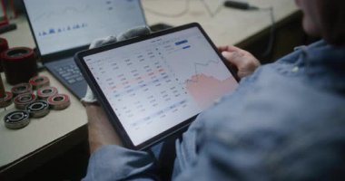 Adam, Dijital Tablet ve Laptop kullanarak Gerçek zamanlı borsa grafiklerini kontrol ediyor. Çalışanların atölyede çalışma saatleri sırasında yatırım yapması, İş ve Çevrimiçi Ticaret 'i birleştirmesi. Kapat..