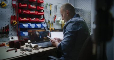 Bilgisayarda Online Ticaret Eğitimi İzleyen İşçi, Akıllı Telefon kullanarak Gerçek Zamanlı Borsa Çizelgelerini İzliyor. Atölyede İnsan Uzaktan Öğrenme Ticaret Günü.