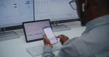 Çevrimiçi Ticaret Uygulaması Kullanılarak Finansal Analizci Gerçek Zamanlı Borsa Çizelgelerini, Akıllı Telefon ve Dijital Ekranları Kontrol Ediyor. Afrikalı Amerikalı İşadamı Yatırım Bankası Ofisi 'nde çalışıyor. Kapat..