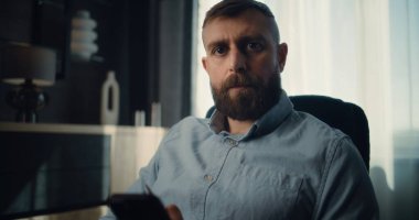 Smartphone üzerinde çalışan Profesyonel Finansal Uzman, Gerçek Zamanlı Hisselerin İzlenmesi, Değişim Piyasası Çizelgeleri, Kameraya Bakma. Yatırım Bankasının Konforlu Ofisinde Başarılı İşadamının Portresi