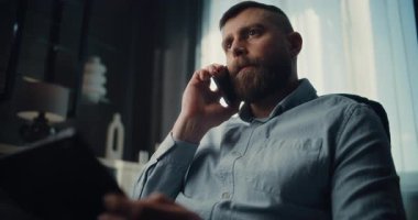 Finansal Uzman İş ortağı veya Yatırımcı ile telefon görüşmesi yapıyor, Tablet Bilgisayar üzerinde çalışıyor, Gerçek zamanlı hisse senetlerini izliyor. Başarılı İşadamı Konforlu Yatırım Bankası Ofisinde Çalışıyor.