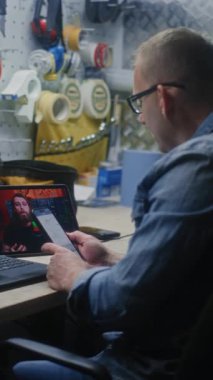 Tamirci Gerçek zamanlı borsa grafiklerini kontrol ediyor, dizüstü bilgisayar ve telefon kullanarak değiş tokuş ediyor, dijital tablet üzerine online ticaret dersi izliyor. Adam atölyede uzaktan ticaret eğitimi alıyormuş. Dikey Çekim.