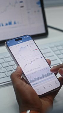 Afro-Amerikan Borsa Analiz Edicisi, Akıllı Telefon ve Tablet Bilgisayar Online Ticari Uygulamasını Kullanarak Gerçek Zamanlı Borsa Çizelgeleri. Ofiste çalışan Yatırım Ajanı. Yakın çekim. Dikey Çekim