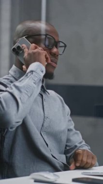 Afrikalı Amerikan Borsacı veya Finansal Analizci Bilgisayarı Kullanıyor ve İş Ortağına Cep Telefonu ile Konuşuyor. Finans Ajansı 'nda çalışan Yatırım Ajanı. Orta boy shot. Dikey Çekim