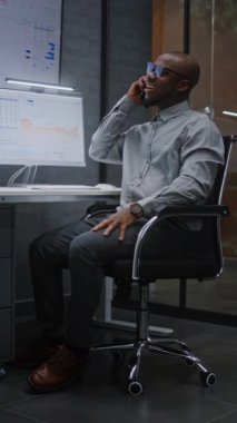 Happy Stock Broker 'ın Gerçek Zamanlı Hisseleri İzlemesi, Ofisteki Çoklu İzleme Bilgisayarında Piyasa Çizelgeleri, Telefonla Konuşma. Başarılı yatırımlar yapan Afro-Amerikan Yatırım Ajanı. Dikey Çekim.