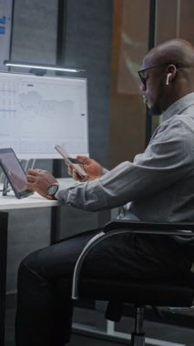 Çoklu Sayısal Aygıtlar ve Bilgisayarda Çoklu Monitör Masaüstü ile Afro-Amerikan Borsası borsası Gerçek-Zaman Hisselerini, Çizelgeleri İzliyor. Ofiste çalışan Yatırım Ajanı. Dikey Çekim.