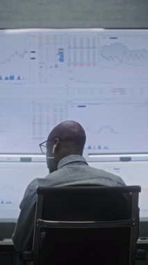 Multi-Monitor Workstation, Real-Time Stocks ve Exchange Market Charts ile bilgisayar üzerinde çalışan bir finans analisti. Afrikalı Amerikalı İşadamı geceleri banka ofisinde çalışıyor. Dikey Çekim.
