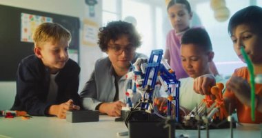 İlkokul öğrencileri masada oturuyor, Robotik Kol Modelini Birlikte Çalışıyorlar. Çok Kültürlü Sınıfta Bilim ve Mühendislik Dersinde Öğretmenlik Eğitimi Grubu. STEM Eğitimi.