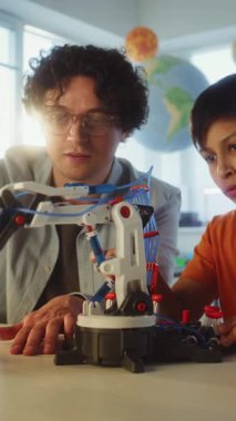 İlkokulda Etkileşimli Öğrenme ve Yaratıcı BTMM Eğitimi: Öğretmenle Robot Silah Çalışan Yetenekli Çocuk. Modern Sınıfta Bilim Dersinde Genç Öğrenci. Dikey Çekim.