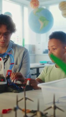 Bilim Dersi: İlköğretim Okulu Öğrenci Robot Kolu Modeli. Modern Sınıfta Akıllı Afro-Amerikan Çocuğu Eğiten Genç Öğretmen. İnteraktif Öğrenme ve BTMM Eğitimi. Dikey Çekim.