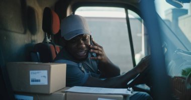 Afro-Amerikan Teslimat Traktörü Arabada Oturuyor, Müşteriyle Cep Telefonu ile Konuşuyor, Çevrimiçi Siparişler, Alış-Verişler, E-Ticaret Ürünleri, Gıda. Kurye Express Teslimat Servisi 'nde çalışıyor..