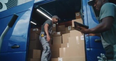 Çoklu Etnik İşçiler Karton Kutuları Çevrimiçi Siparişlerle Boşaltıyorlar, Teslimat Kamyonundan E-Ticari Mallar. Afro-Amerikan Yöneticisi Tablet Bilgisayar kullanıyor. Lojistik Perakende Deposu 'nun dışında çalışıyorum..