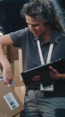 Lojistik Deposu 'nun dışında çeşitli çalışanlar karton kutularla nakliye kamyonu yüklüyor, online siparişler, e-ticaret ürünleri. Dijital Tablet ve Barkod Tarayıcı kullanan Kadın Yönetici. Dikey Çekim.