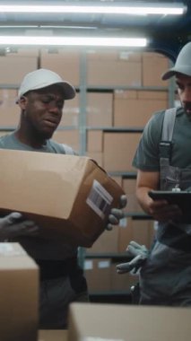 Lojistik Perakende Deposu 'nun dışında muhtelif çalışanlar karton kutularla kargo kamyonu boşaltıyorlar. Dijital Tablet kullanarak Yönetici Tarayıcı Paketleri. Çevrimiçi Siparişler, E-Ticaret Malzemeleri. Dikey Çekim.