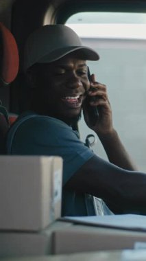 Afro-Amerikan Nakliye Aracı Şoförü Müşteriyle Telefonla Konuşuyor, Evrakları Dolduruyor, Çevrimiçi Siparişler Veriyor, E-Ticari Mallar. Express Teslimat Servisi 'nde çalışan adam. Dikey Çekim.