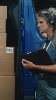 Lojistik Deposu 'nun dışında, Afro-Amerikan çalışanı kadın envanter müdürüyle birlikte karton kutularla teslimat kamyonu boşaltıyor. Çevrimiçi Siparişler, E-Ticaret Malzemeleri. Teslimat servisi. Dikey Çekim.