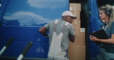 Lojistik Dağıtım Deposu 'nun dışında Afro-Amerikan çalışanı, kadın envanter müdürüyle birlikte karton kutularla teslimat kamyonu boşaltıyor. Çevrimiçi Siparişler ve E-Ticaret Malzemeleri. Kargo Servisi