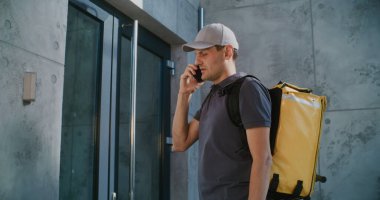 Teslimatçı Modern Ofis 'in yanında duruyor, Müşteriye Telefonla Başarılı Teslimat' ı bildiriyor. Restorandan iş kadınlarına yemek getiren adam, yemek dağıtım servisinde çalışıyor. Yavaş Hareket.