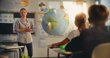 İlkokul kızı, Dünya Modelini Kullanarak Sınıfın Önündeki Yeşil Enerji Kaynaklarını Sunar. Çevre Bilimi dersinde Zeki Çeşitli Çocukları Eğiten Kadın Öğretmenler Dersi. STEM Eğitimi.