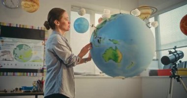 Yenilenebilir Enerji BTMM Sınıfı: Sınıfta Dünya Gezegeni Modelini Kullanarak Bilim ve Enerji Kaynaklarını Açıklayan Kadın Öğretmen. Dünya 'daki Rüzgâr Türbinleri ve Güneş Panelleri' nin minyatür 3D modelleri. Orta Çekim.