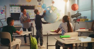 İlkokul çocuğu, Dünya Modelini Kullanarak Sınıfın Önündeki Yeşil Enerji Kaynaklarını Sunar. Çok Irklı Sınıfta Bilim Dersinde Akıllı Çocukları Eğiten Bayan Öğretmen. BTMM Eğitim. Doli Vuruşu.