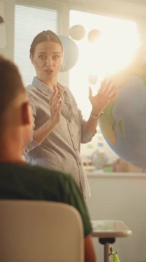 BTMM Yenilenebilir Enerji Sınıfı: Dünya Modelini Kullanan İlkokul Öğrencilerine Enerji Kaynaklarını Açıklayan Kadın Öğretmen. Sınıfta Coğrafya Öğrenen Çeşitli Çocuklar. Dolly Shot. Dikey Çekim.