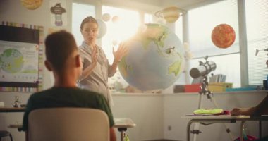 BTMM Yenilenebilir Enerji Sınıfı: Dünya Modelini Kullanan İlkokul Öğrencilerine Enerji Kaynaklarını Açıklayan Kadın Öğretmen. Modern Sınıfta Çeşitli Çocuklar Coğrafya ve Bilim Öğreniyor. Doli Vuruşu