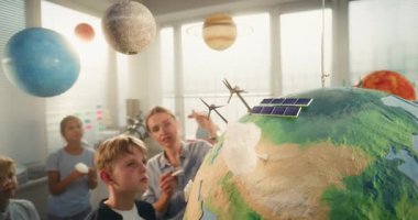 Çevre Bilimi Dersi: Çok Etnik Sınıfta Zeki Çocuklar Takımına Yenilenebilir Enerji Eğiten Kadın Öğretmen. İlkokul çocuğu Dünya Modeline Minyatür Bulut Ekliyor. STEM Eğitimi.