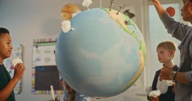 STEM Yenilenebilir Enerji Dersi: Akıllı Çeşitli Çocukları Eğiten Kadın Öğretmen Dünya 'yı Minyatür 3 boyutlu Rüzgar Türbinleri ve Güneş Panelleri Modelleri ile Kullanıyor. İlkokul çocukları fen eğitimi alıyor. Kapat..