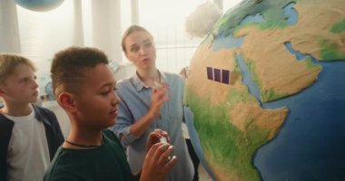 Bilim BTMM Dersi: Çok Etnik Sınıfta Zeki Çocuklar Takımına Yenilenebilir Enerji Eğiten Kadın Öğretmen. Afrikalı Amerikalı okul çocuğu Dünya Modeline Minyatür Güneş Paneli Ekliyor. Kapat..