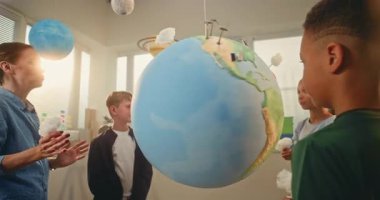 Yenilenebilir Enerji BTMM Sınıfı: Modern Sınıfta Akıllı Çocuklar Ekibine Bilim ve Enerji Kaynaklarını Açıklayan Kadın Öğretmen. İlkokul öğrencileri Dünya 'ya Bulutların Minyatür Modelleri Ekliyor.