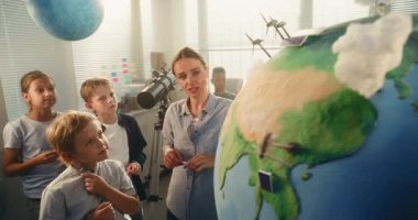 Ekoloji BTMM Sınıfı: İlkokul çocuğu Dünya 'ya Rüzgâr Türbininin Minyatür Modelini Ekliyor. Fen Bilgisi ve Yenilenebilir Enerji Kaynaklarını Modern Sınıftaki Zeki Öğrencilere Açıklayan Bayan Öğretmen.