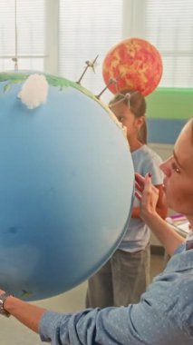 Bilim Dersi: Çok Irklı Sınıfta Akıllı Çocuklara Yenilenebilir Enerji Eğitimi Yapan Kadın Öğretmen. Minyatür Bulutları Dünya Modeline Bağlayan İlkokul Çocukları. BTMM Eğitim. Dikey Çekim.