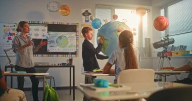 İlkokul çocuğu, Dünya Modelini Kullanarak Sınıfın Önündeki Yeşil Enerji Kaynaklarını Sunar. Çok Irklı Sınıfta Bilim Dersinde Akıllı Çocukları Eğiten Bayan Öğretmen. BTMM Eğitim. Yavaş Hareket.