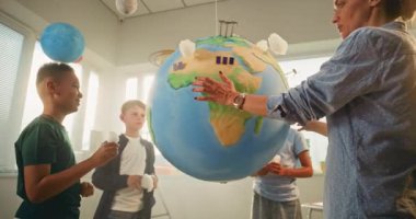 Yenilenebilir Enerji BTMM Sınıfı: Modern Sınıfta Çeşitli Çocuklar Takımına Bilim ve Enerji Kaynaklarını Açıklayan Kadın Öğretmen. İlkokul öğrencileri Dünya 'ya Bulutların Minyatür Modelleri Ekliyor.