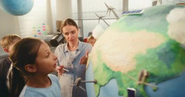 Ekoloji BTMM Sınıfı: İlköğretim Okulu Kızı Cloud to Globe 'un Minyatür Modelini Bağlıyor. Fen Bilgisi ve Yenilenebilir Enerji Kaynaklarını Modern Sınıftaki Akıllı Öğrencilere Açıklayan Bayan Öğretmen. Kapat..